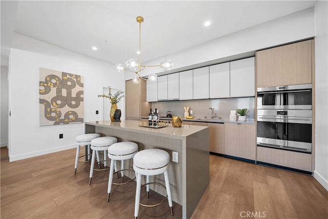 kitchen featuring sink, stainless steel double oven, decorative light fixtures, and light wood-type flooring