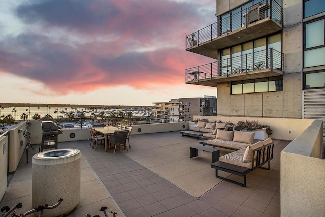 patio terrace at dusk with an outdoor living space, a grill, and a water view