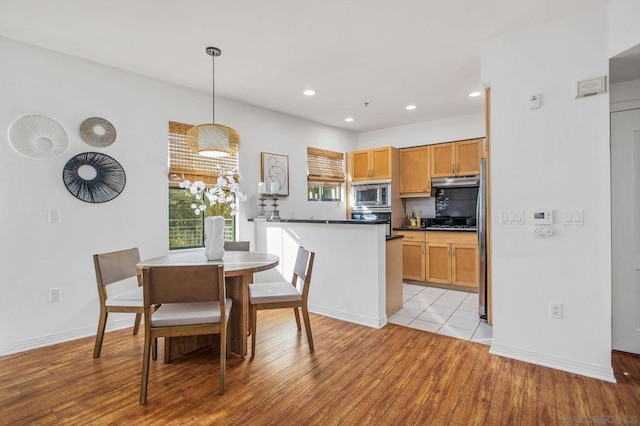 kitchen with light wood-type flooring, appliances with stainless steel finishes, and pendant lighting