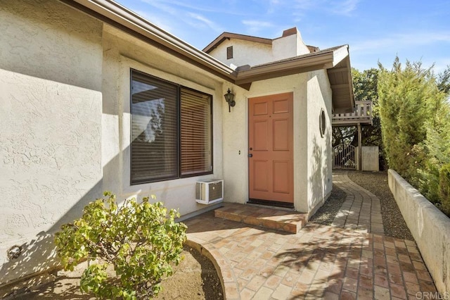 view of exterior entry with a wall mounted air conditioner and a patio