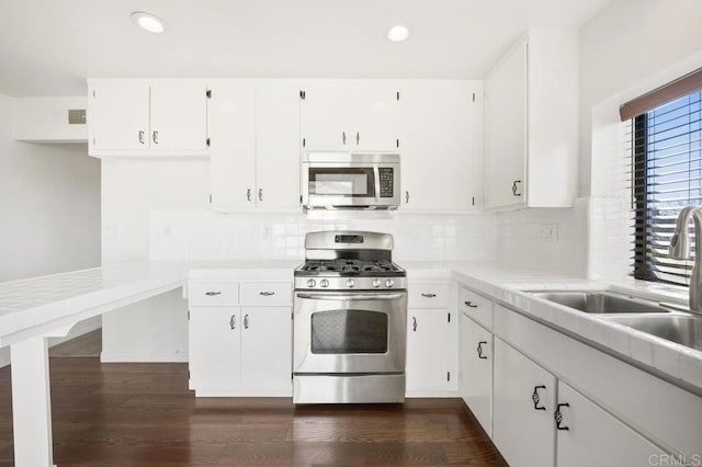 kitchen with sink, dark hardwood / wood-style floors, decorative backsplash, appliances with stainless steel finishes, and white cabinetry