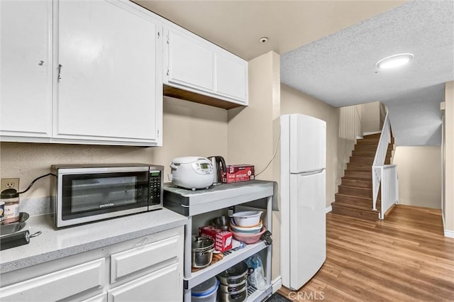 kitchen with white cabinets, a textured ceiling, light wood-type flooring, and white fridge