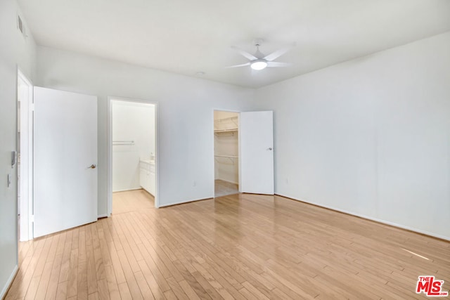 unfurnished bedroom with ensuite bath, a spacious closet, ceiling fan, light hardwood / wood-style flooring, and a closet