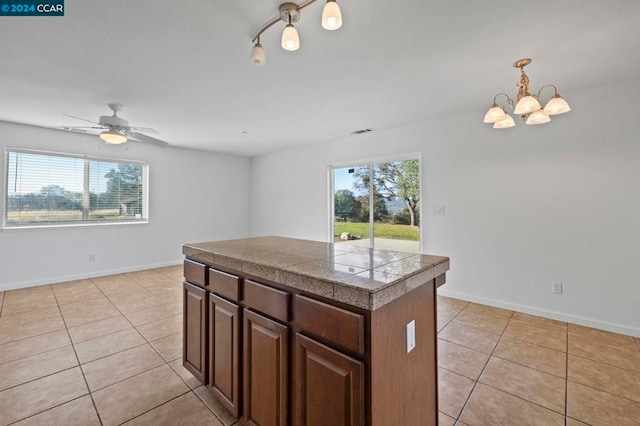 kitchen with pendant lighting, ceiling fan with notable chandelier, a kitchen island, and light tile patterned flooring