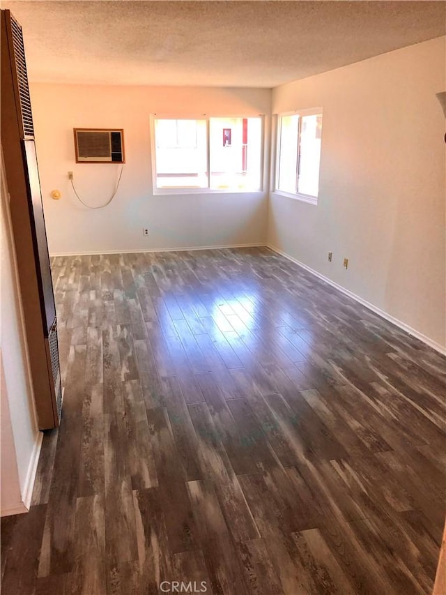 empty room with a wall mounted air conditioner, dark hardwood / wood-style flooring, and a textured ceiling