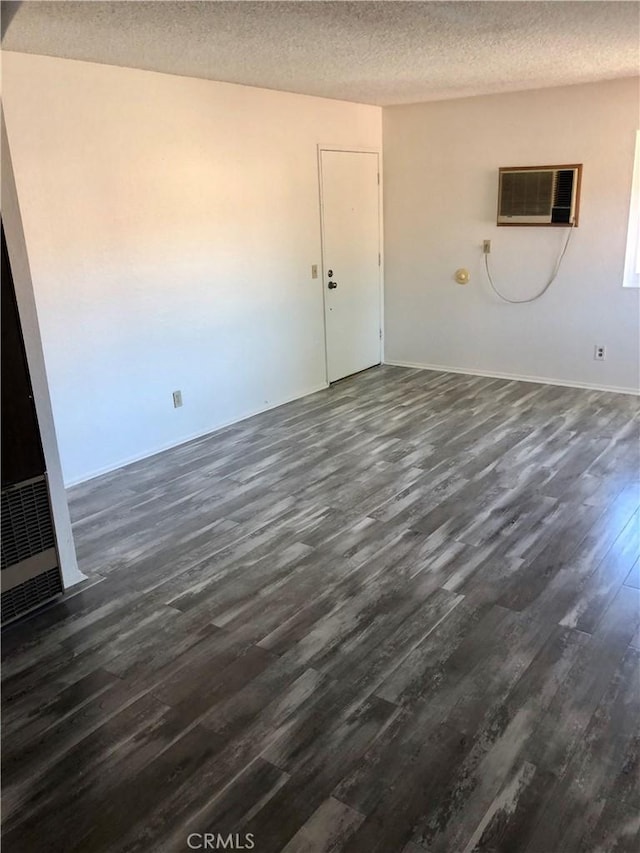 empty room featuring a textured ceiling, dark wood-type flooring, and a wall unit AC