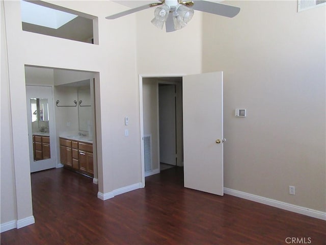 unfurnished bedroom with ceiling fan, dark hardwood / wood-style floors, a high ceiling, and a skylight