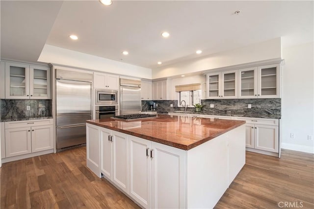 kitchen with built in appliances, a center island, dark stone countertops, and light hardwood / wood-style floors