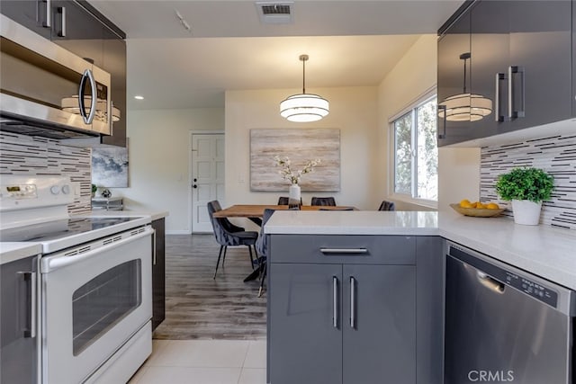 kitchen with kitchen peninsula, backsplash, stainless steel appliances, light hardwood / wood-style floors, and hanging light fixtures