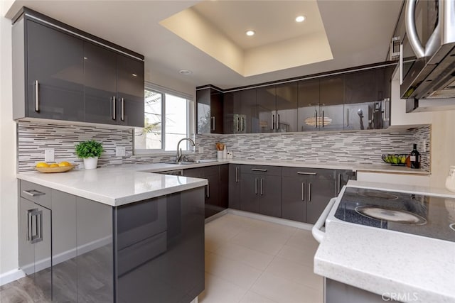 kitchen with light stone countertops, tasteful backsplash, dark brown cabinetry, a tray ceiling, and sink