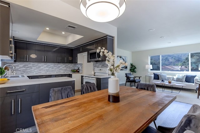 dining area with a raised ceiling, sink, and light hardwood / wood-style floors