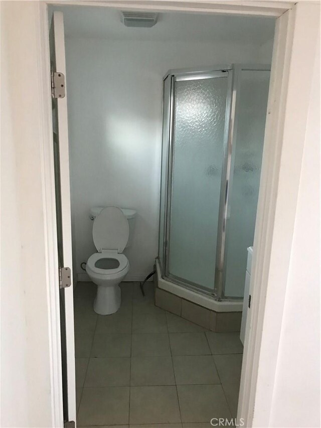 bathroom with tile patterned flooring, toilet, and a shower with door