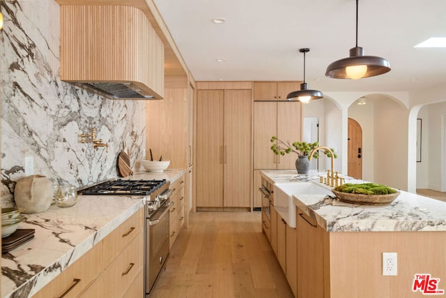 kitchen featuring light brown cabinets, a kitchen island with sink, sink, stainless steel stove, and light wood-type flooring