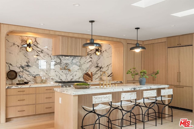 kitchen with decorative light fixtures, light brown cabinetry, and a skylight