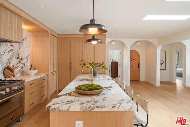 kitchen with hanging light fixtures, light stone counters, light hardwood / wood-style floors, a kitchen island with sink, and high end stainless steel range