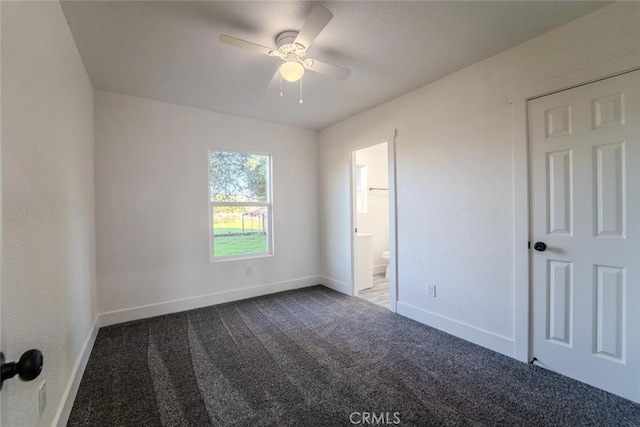 interior space with ensuite bath, dark carpet, and ceiling fan