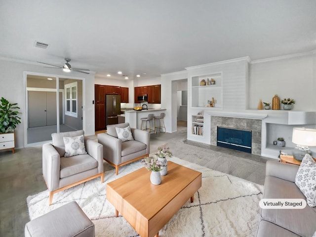 living room with a fireplace, ceiling fan, ornamental molding, and built in features