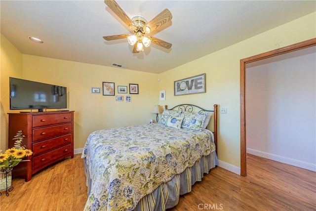 bedroom with a ceiling fan, wood finished floors, visible vents, and baseboards