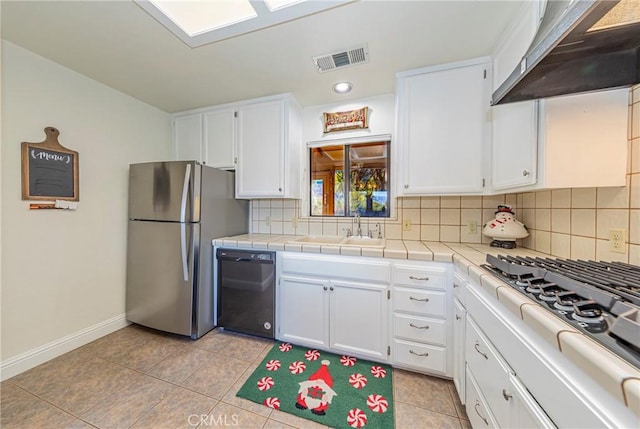 kitchen featuring white cabinets, wall chimney exhaust hood, stainless steel appliances, and tile countertops