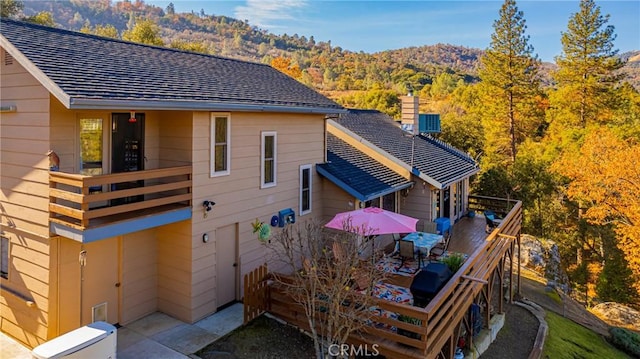 back of property with a balcony, a shingled roof, and a view of trees