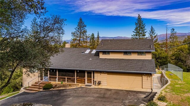 view of front of house with aphalt driveway, a chimney, a shingled roof, a mountain view, and fence