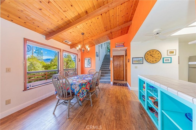 dining space featuring lofted ceiling with beams, stairway, wood finished floors, and ceiling fan with notable chandelier