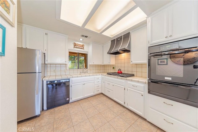 kitchen featuring tile counters, freestanding refrigerator, oven, dishwasher, and wall chimney exhaust hood