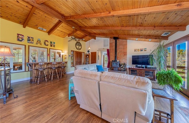 living area with a wood stove, visible vents, beamed ceiling, and wood finished floors