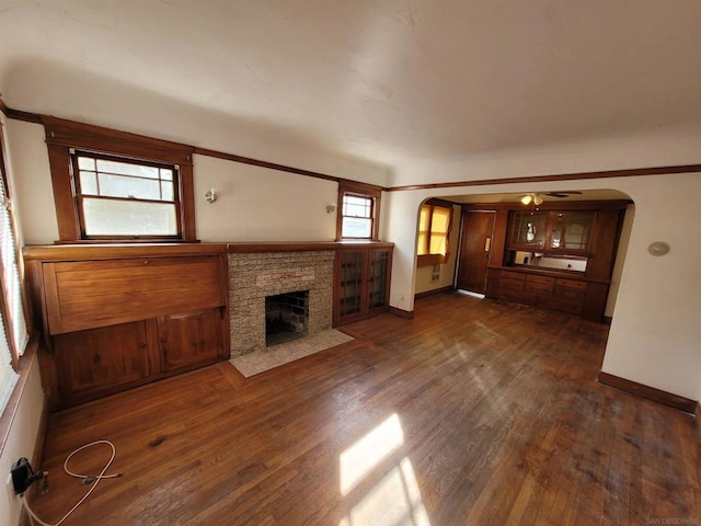 unfurnished living room with dark hardwood / wood-style flooring, a fireplace, ornamental molding, and ceiling fan