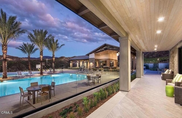 pool at dusk featuring a mountain view and a patio