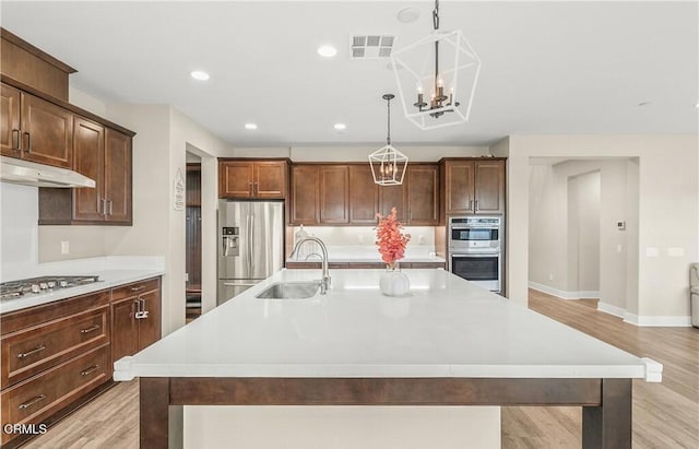 kitchen with sink, light hardwood / wood-style floors, decorative light fixtures, a center island with sink, and appliances with stainless steel finishes