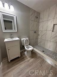 bathroom with toilet, hardwood / wood-style floors, vanity, and tiled shower