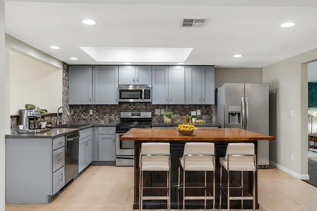 kitchen featuring appliances with stainless steel finishes, backsplash, a breakfast bar, sink, and butcher block countertops