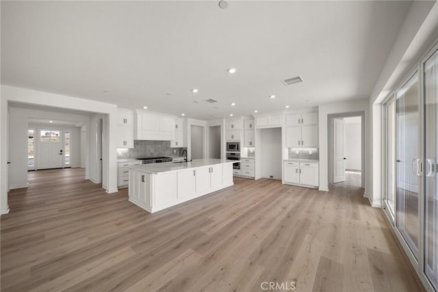 kitchen featuring visible vents, decorative backsplash, white cabinets, stainless steel microwave, and light wood-type flooring