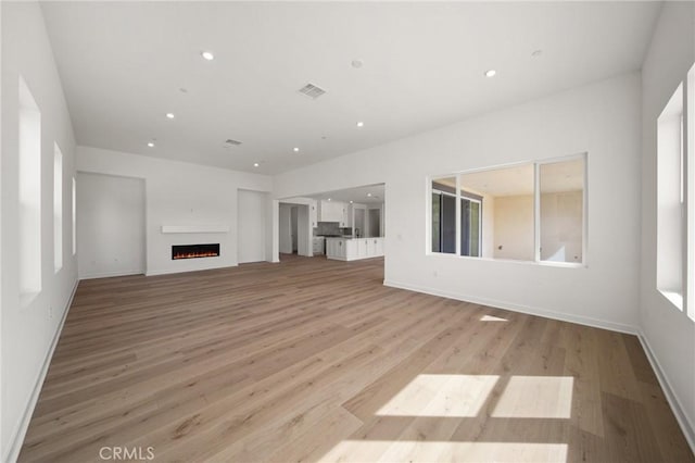 unfurnished living room with light wood-type flooring, a lit fireplace, and recessed lighting