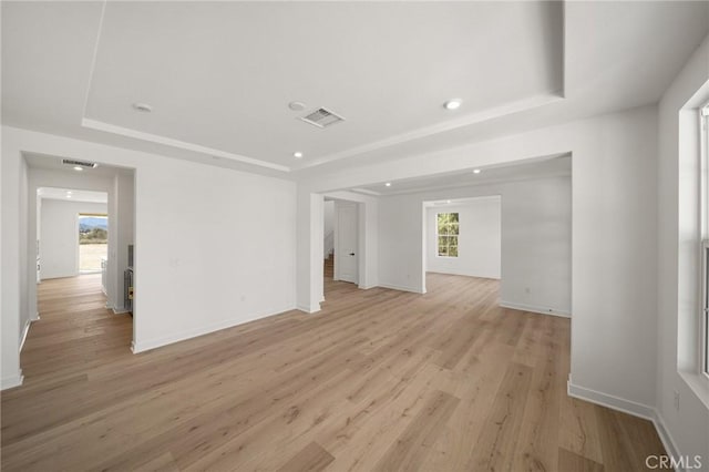 unfurnished room featuring light wood-style floors, a tray ceiling, visible vents, and baseboards