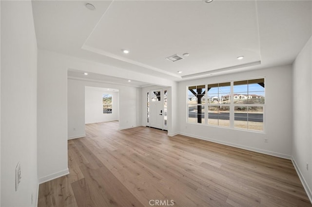 empty room featuring a healthy amount of sunlight, light wood-style flooring, baseboards, and a raised ceiling