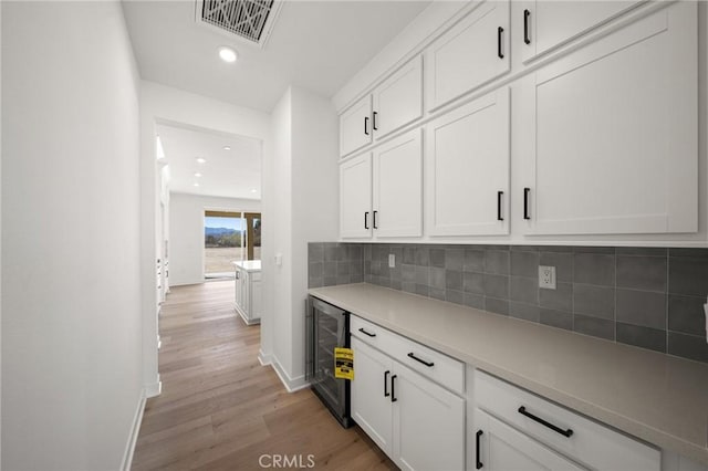 bar featuring visible vents, decorative backsplash, baseboards, light wood-style flooring, and wine cooler