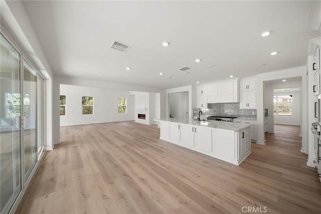 kitchen with a fireplace, tasteful backsplash, visible vents, open floor plan, and white cabinets