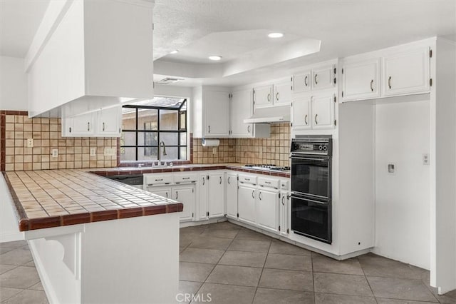 kitchen with white cabinetry, a tray ceiling, tile counters, and kitchen peninsula