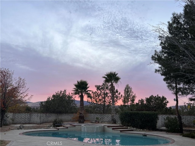 pool at dusk with an in ground hot tub and a mountain view