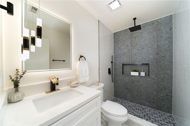 bathroom featuring a tile shower, vanity, and toilet