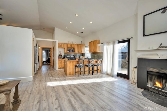 kitchen with a kitchen bar, high vaulted ceiling, kitchen peninsula, stainless steel appliances, and a tiled fireplace