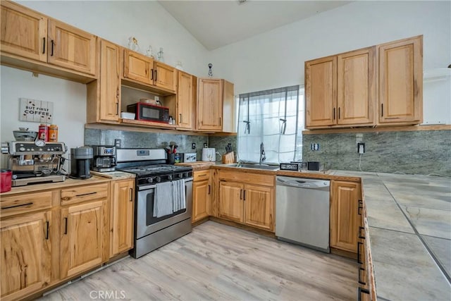 kitchen with sink, tile countertops, vaulted ceiling, stainless steel appliances, and backsplash