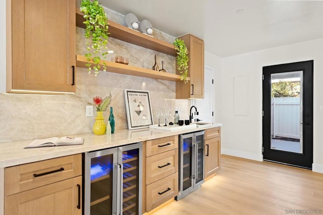 bar with light brown cabinets, light wood-type flooring, sink, and beverage cooler