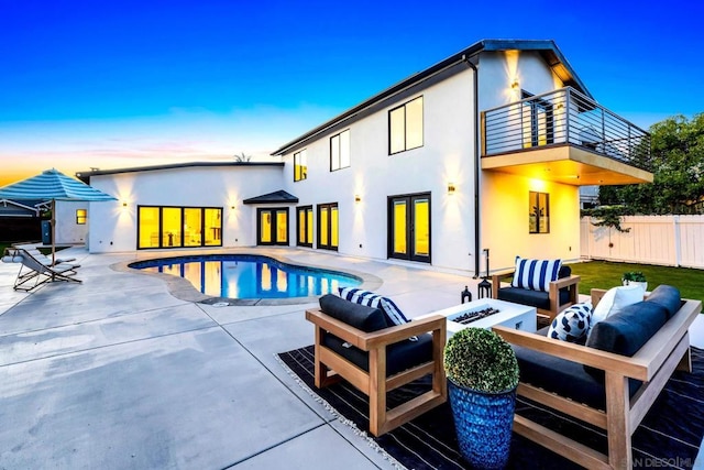 back house at dusk with a balcony, a patio area, an outdoor living space with a fire pit, and a fenced in pool