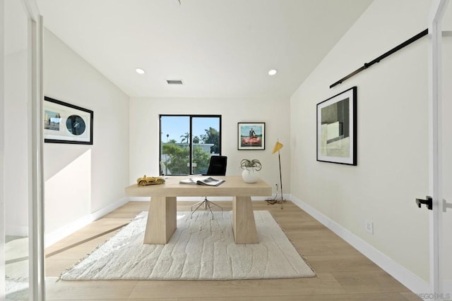 office featuring a barn door, light hardwood / wood-style flooring, and vaulted ceiling