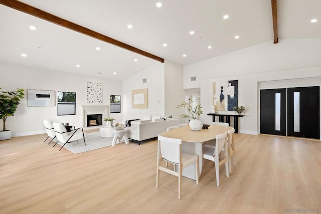 dining space with beam ceiling, light wood-type flooring, and high vaulted ceiling