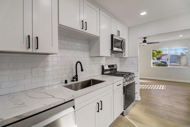 kitchen with sink, light wood-type flooring, appliances with stainless steel finishes, light stone counters, and white cabinetry