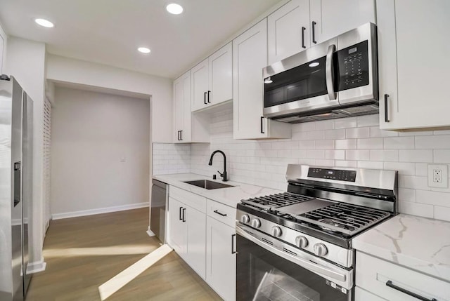 kitchen with white cabinets, sink, light wood-type flooring, appliances with stainless steel finishes, and light stone counters